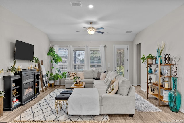 living room featuring lofted ceiling, ceiling fan, light wood-style flooring, visible vents, and a glass covered fireplace