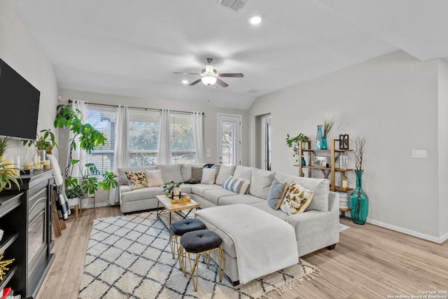 living area with baseboards, a glass covered fireplace, lofted ceiling, ceiling fan, and light wood-type flooring