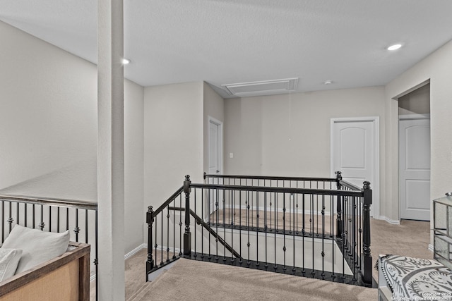 interior space featuring attic access, baseboards, carpet, a textured ceiling, and an upstairs landing