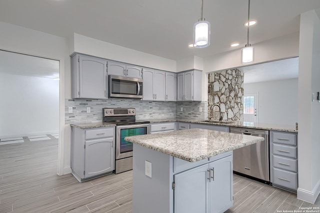 kitchen with appliances with stainless steel finishes, decorative backsplash, a sink, and gray cabinetry