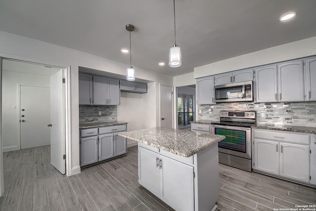 kitchen featuring light stone counters, stainless steel appliances, wood finish floors, a kitchen island, and backsplash