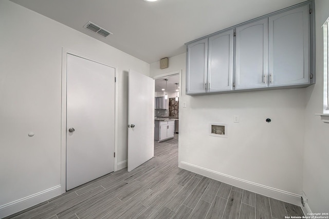 clothes washing area with wood finish floors, hookup for a washing machine, visible vents, cabinet space, and baseboards