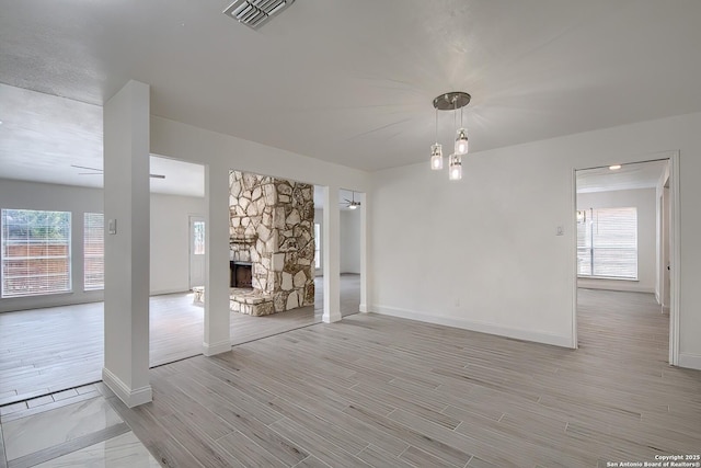 unfurnished room with light wood-style flooring, visible vents, baseboards, and a stone fireplace