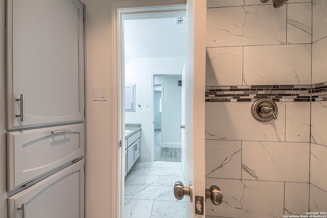 full bath featuring marble finish floor, tiled shower, and vanity