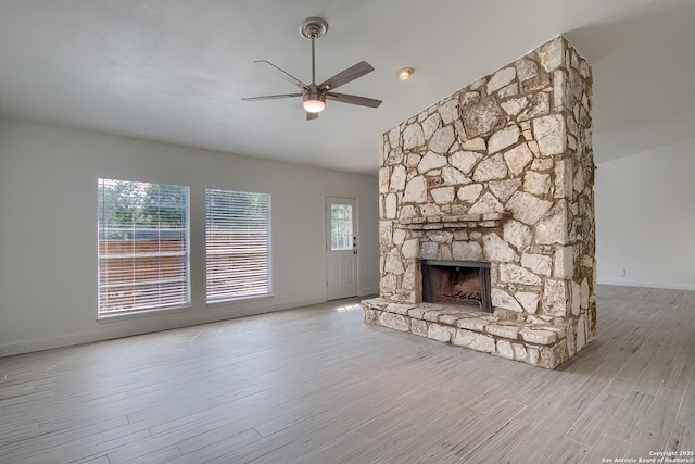 unfurnished living room with a ceiling fan, a stone fireplace, baseboards, and wood finished floors