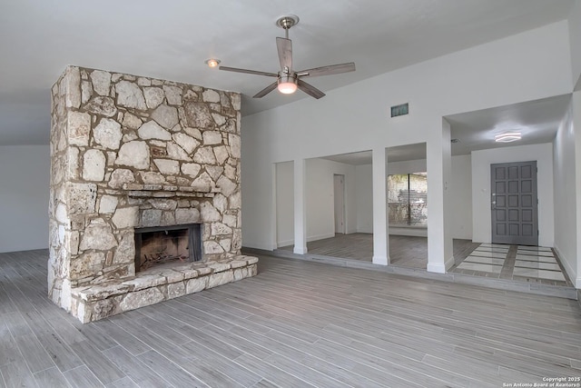 unfurnished living room with visible vents, a ceiling fan, a stone fireplace, wood finished floors, and baseboards