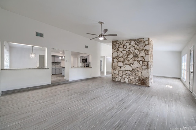 unfurnished living room featuring visible vents, light wood-style flooring, ceiling fan, high vaulted ceiling, and baseboards