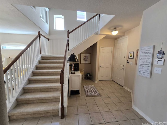 foyer entrance with stairway, a towering ceiling, light tile patterned flooring, a textured ceiling, and baseboards