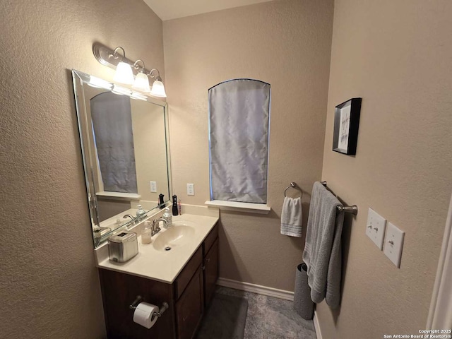 bathroom with a textured wall, vanity, and baseboards