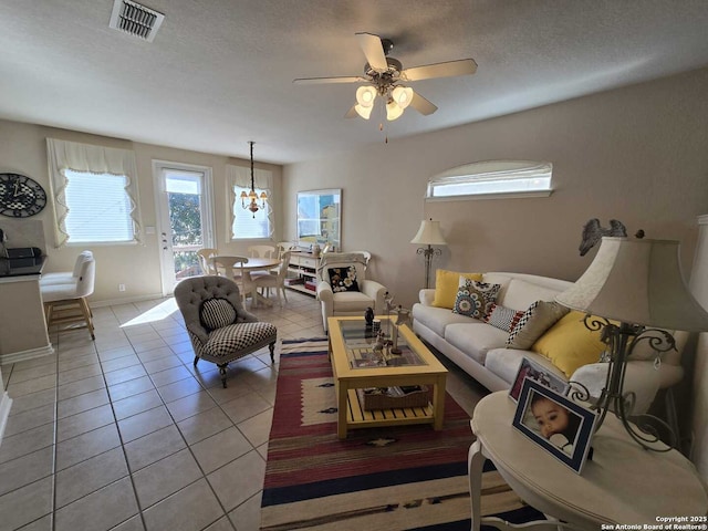 living area with light tile patterned floors, visible vents, a ceiling fan, a textured ceiling, and baseboards