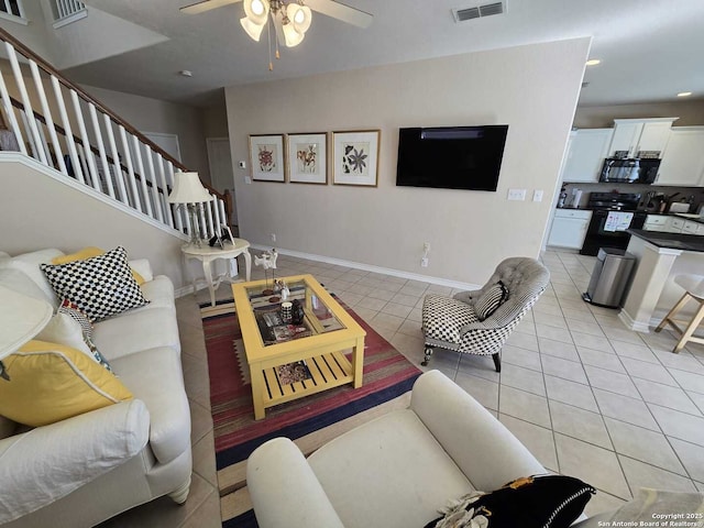 living area featuring light tile patterned floors, visible vents, ceiling fan, baseboards, and stairs