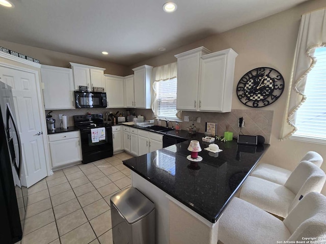 kitchen with light tile patterned floors, white cabinets, a peninsula, black appliances, and a sink