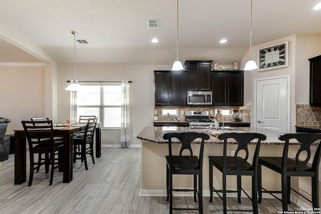 kitchen with a kitchen bar, visible vents, stainless steel appliances, and decorative backsplash