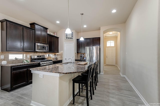 kitchen with a kitchen bar, appliances with stainless steel finishes, arched walkways, and decorative backsplash