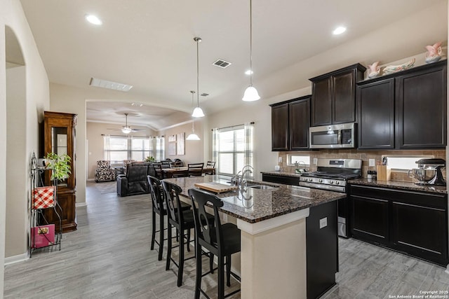 kitchen with stainless steel appliances, a sink, open floor plan, a wealth of natural light, and dark stone counters