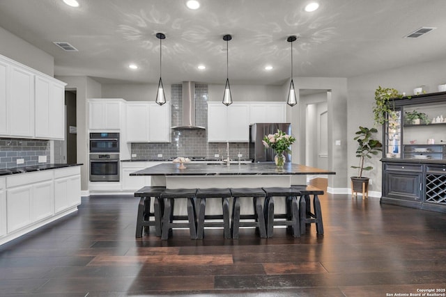 kitchen featuring visible vents, wall chimney range hood, dark countertops, and appliances with stainless steel finishes