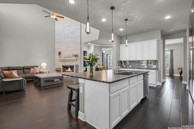 kitchen featuring a kitchen island with sink, dark wood-type flooring, a sink, open floor plan, and dark countertops