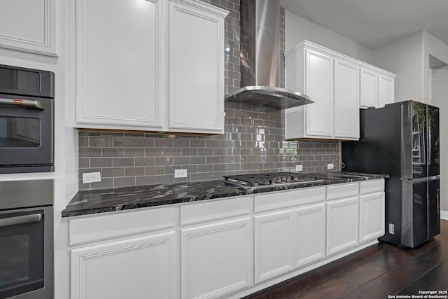 kitchen with wall chimney range hood, backsplash, appliances with stainless steel finishes, and white cabinetry