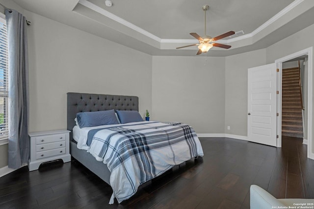 bedroom with dark wood-style floors, a raised ceiling, baseboards, and a ceiling fan