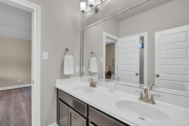 bathroom with wood finished floors, a sink, baseboards, and double vanity