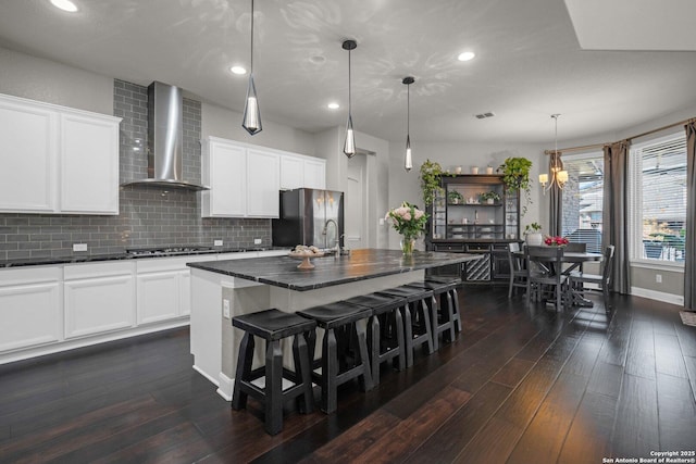 kitchen with stainless steel appliances, dark wood-style flooring, wall chimney exhaust hood, tasteful backsplash, and dark countertops