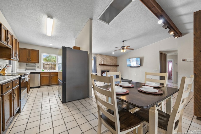 dining room with lofted ceiling with beams, ceiling fan, a textured ceiling, light tile patterned flooring, and a fireplace