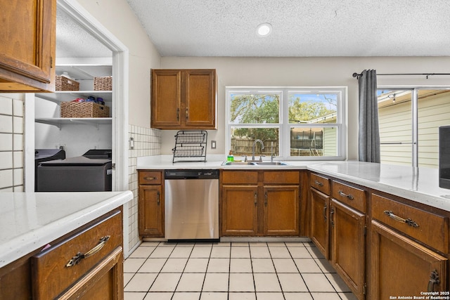 kitchen featuring brown cabinetry, dishwasher, a textured ceiling, a sink, and light tile patterned flooring