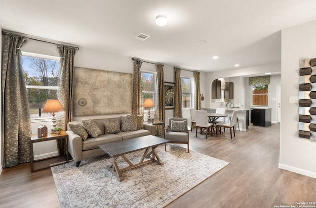 living room featuring light wood-style flooring, visible vents, arched walkways, and a wealth of natural light