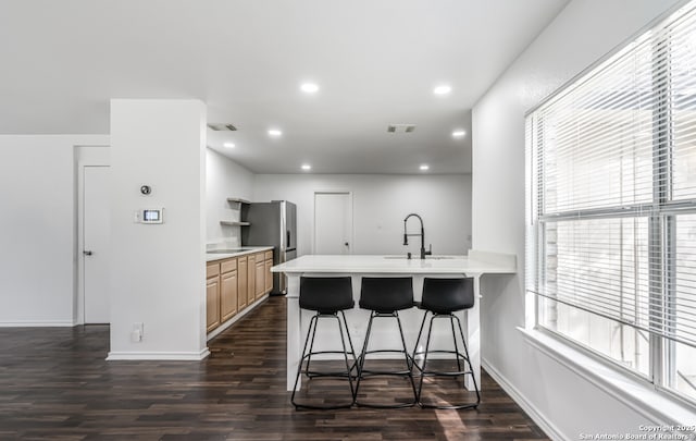 kitchen with light countertops, a breakfast bar, stainless steel fridge, and a sink