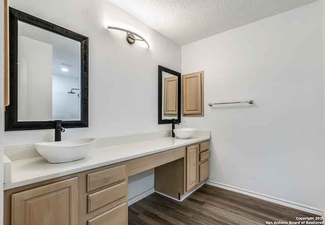 full bathroom featuring double vanity, a sink, a textured ceiling, and wood finished floors