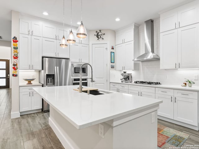 kitchen featuring backsplash, a kitchen island with sink, stainless steel appliances, wall chimney range hood, and a sink