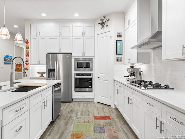 kitchen featuring appliances with stainless steel finishes, white cabinetry, a sink, and wall chimney exhaust hood