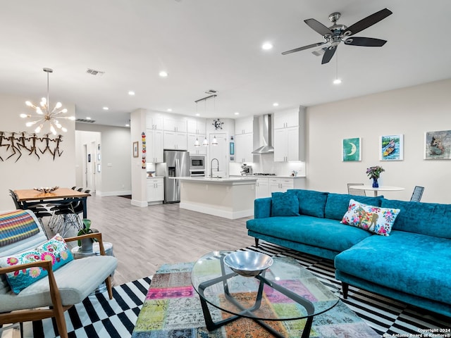 living area with light wood-style flooring, ceiling fan with notable chandelier, baseboards, and recessed lighting