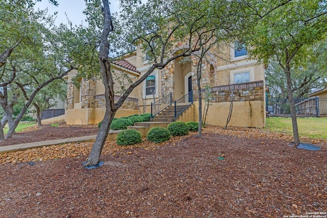 view of front of home featuring stone siding, a tiled roof, fence, and stucco siding