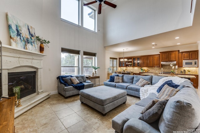 living area featuring baseboards, light tile patterned flooring, crown molding, a fireplace, and ceiling fan with notable chandelier