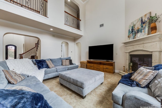 tiled living area with arched walkways, a premium fireplace, visible vents, ornamental molding, and stairway