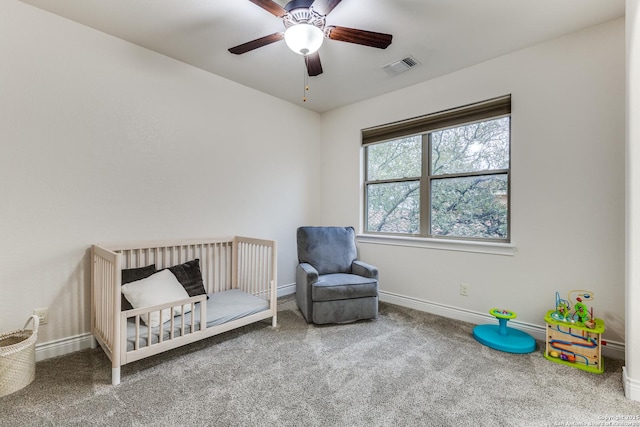 carpeted bedroom with a crib, a ceiling fan, visible vents, and baseboards