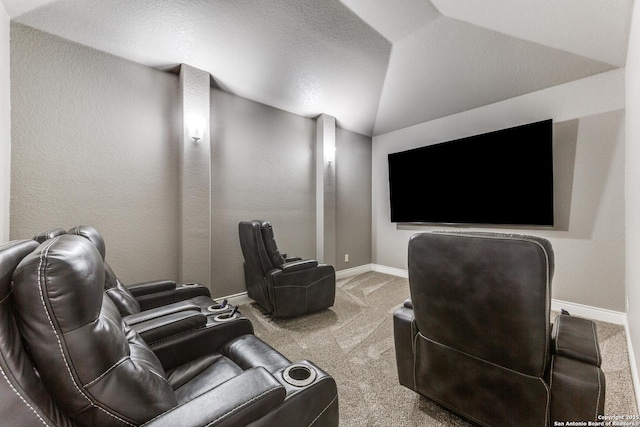 carpeted cinema room with a textured wall, vaulted ceiling, and baseboards