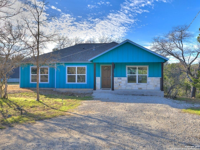 view of front of property with board and batten siding, stone siding, roof with shingles, and driveway