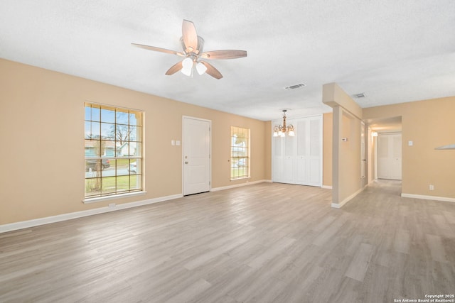 unfurnished living room featuring ceiling fan with notable chandelier, baseboards, visible vents, and light wood-style floors