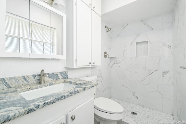 full bathroom featuring tiled shower, vanity, and toilet