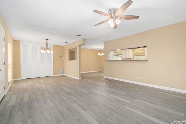 unfurnished living room with baseboards, visible vents, wood finished floors, and ceiling fan with notable chandelier