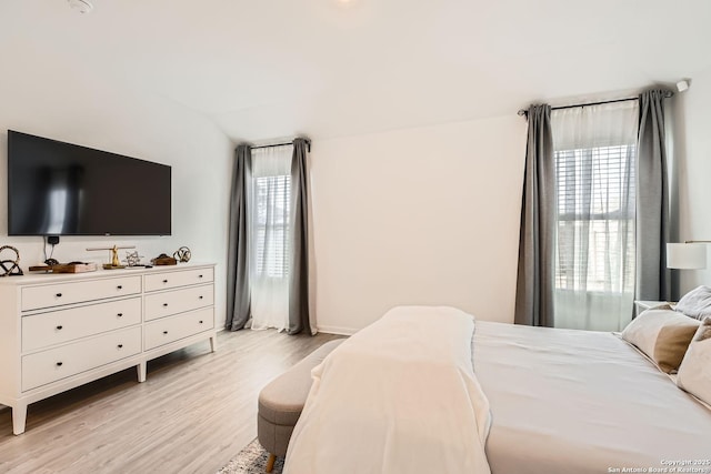 bedroom featuring lofted ceiling, multiple windows, and light wood finished floors