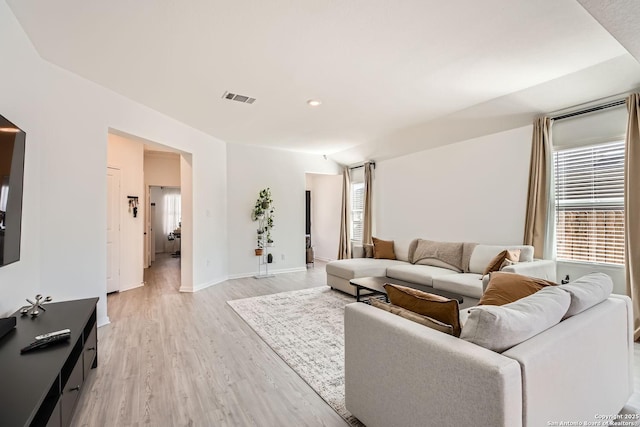 living room with lofted ceiling, light wood-style flooring, visible vents, and baseboards