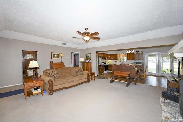 living room featuring light carpet, visible vents, a textured ceiling, and ceiling fan with notable chandelier