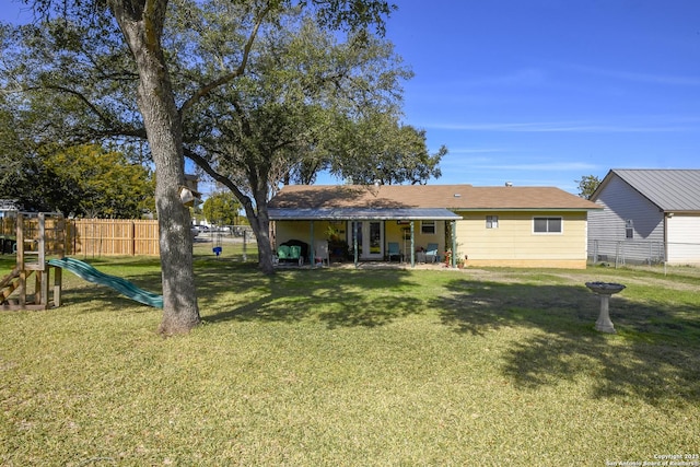 back of house with a playground, fence, and a lawn