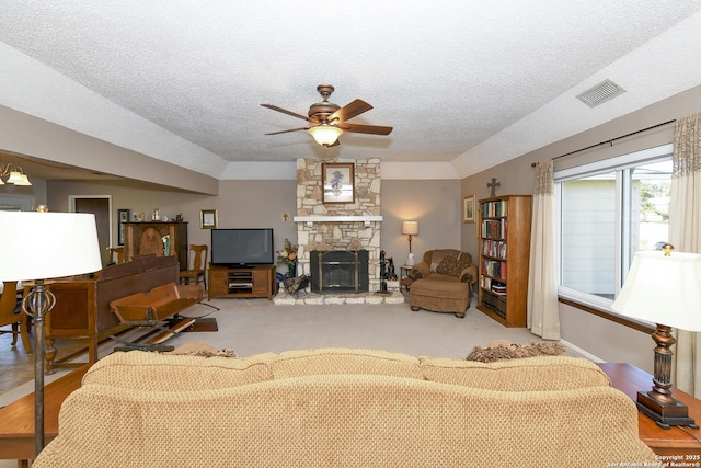 living room featuring ceiling fan, visible vents, a textured ceiling, and a stone fireplace