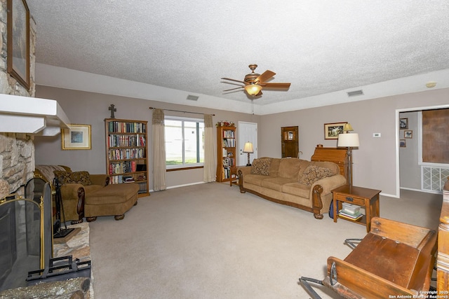 carpeted living room with ceiling fan, visible vents, a textured ceiling, and a stone fireplace