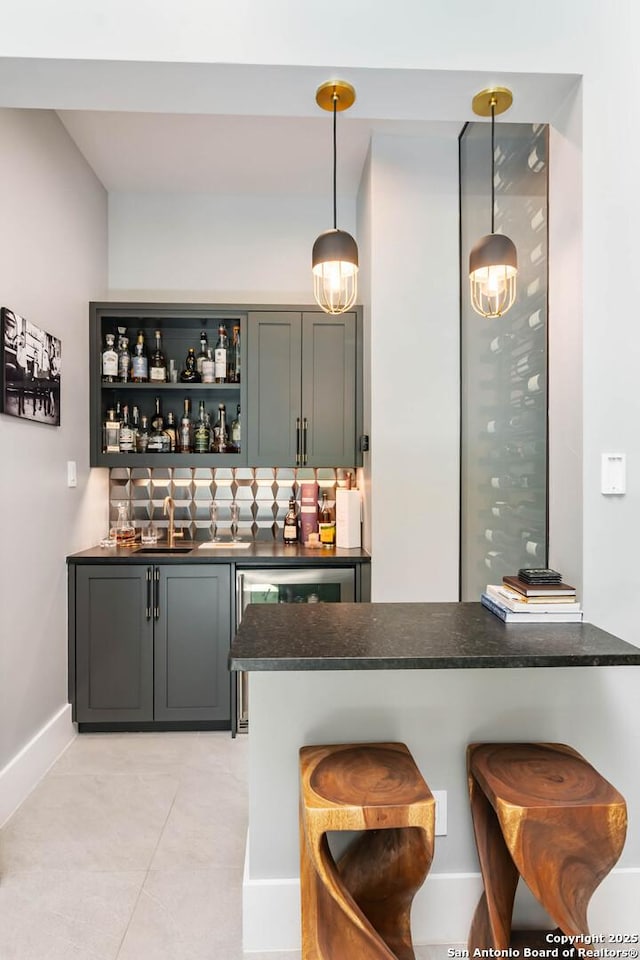 bar with light tile patterned floors, a sink, decorative backsplash, wet bar, and decorative light fixtures