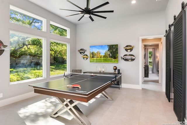 game room featuring light tile patterned floors, a high ceiling, a barn door, a ceiling fan, and baseboards